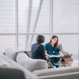 Une médecin est assise sur le canapé de son cabinet avec une patiente.