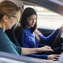 Fahrlehrerin erklärt Fahrschülerin den Aufbau des Autos.