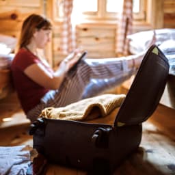 A young woman has packed a suitcase and is booking a flight.