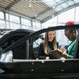 Young woman buys her first car from car dealer in a car garage.