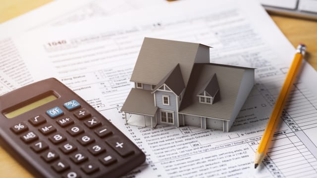 A model house, a calculator and a pencil are on a mortgage calculation.