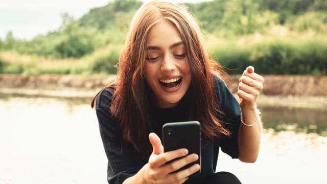 A woman looks happy about something she has seen on her mobile phone. 