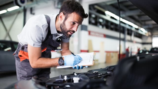 Ein Mann untersucht die Motorhaube eines Autos 