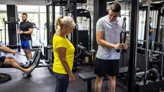 Eine Trainerin erklärt einem Kunden ein Gerät im Fitnessstudio.