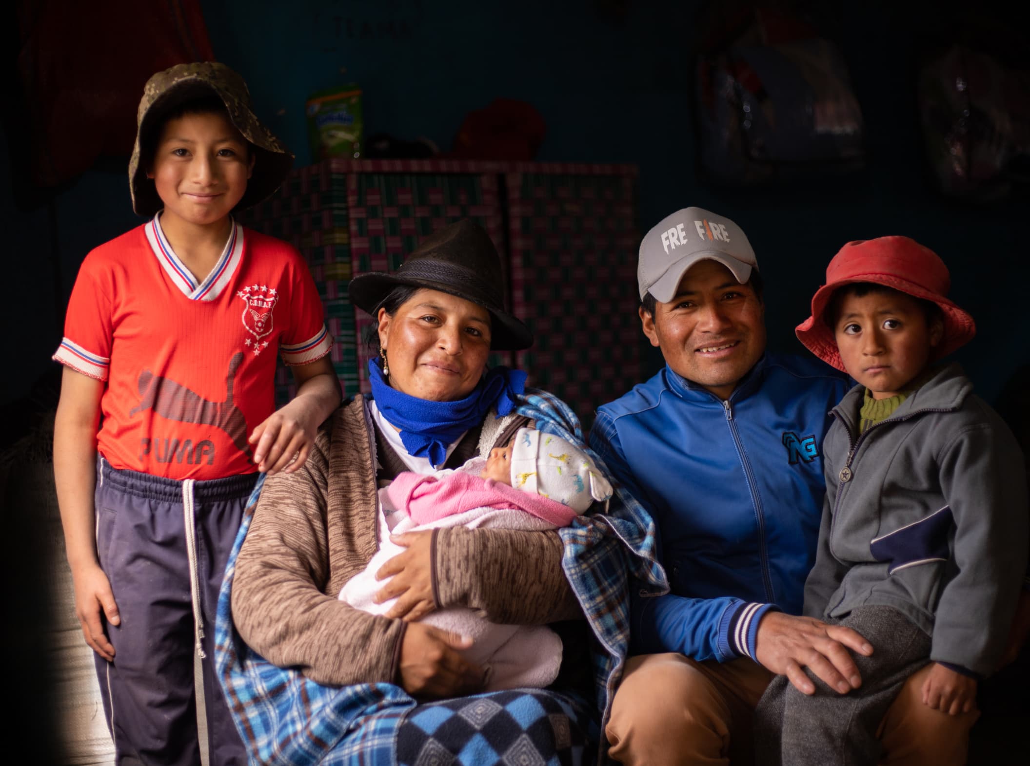A South American Family of 5 sits together in their house. Light shines through the darkness onto their smiling faces