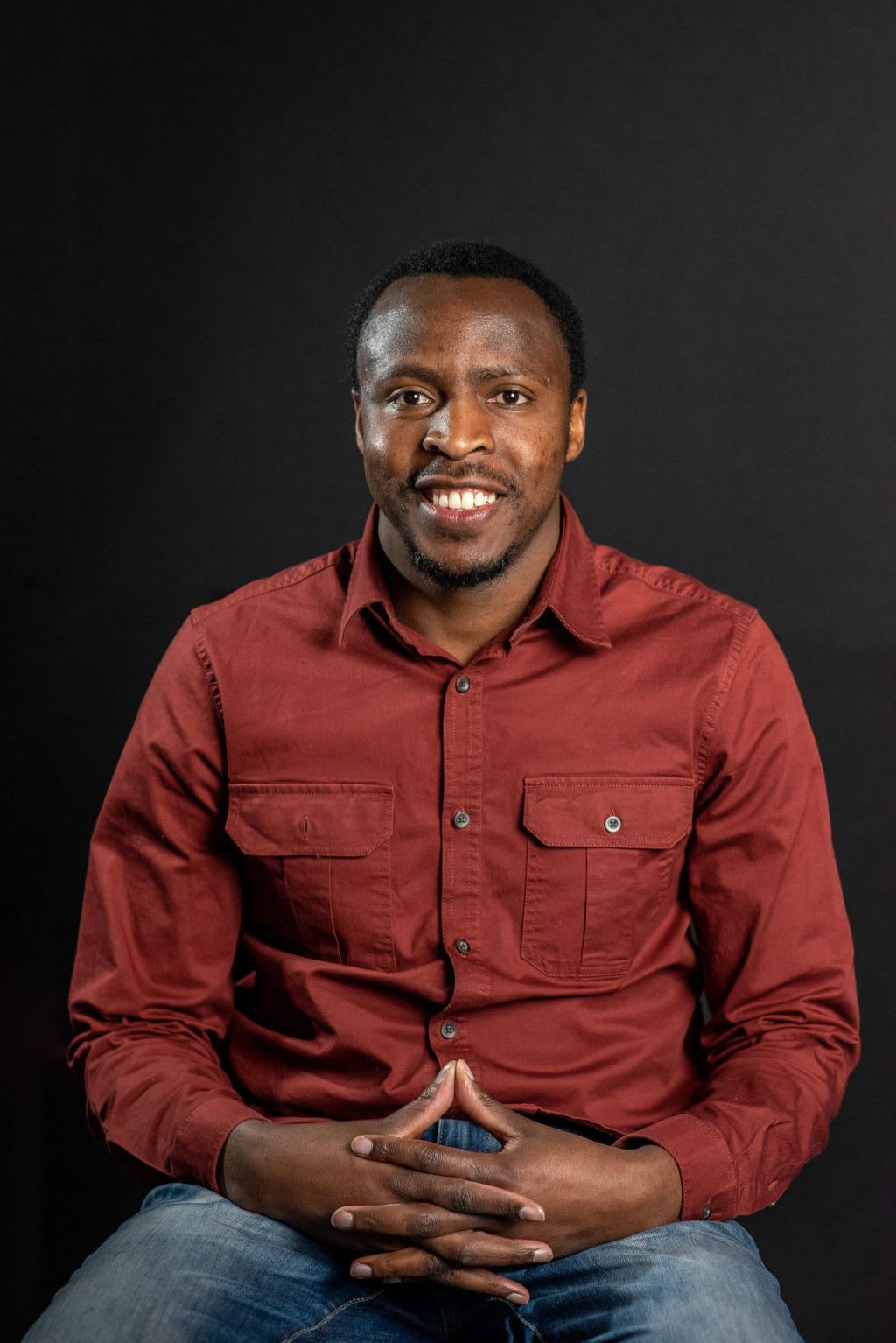 Martin, a Ugandan alumni, sits with hands crossed, smiling