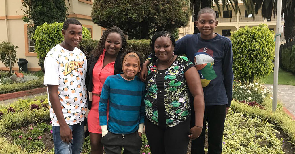 A family stands together outside, smiling, with their arms around each other.