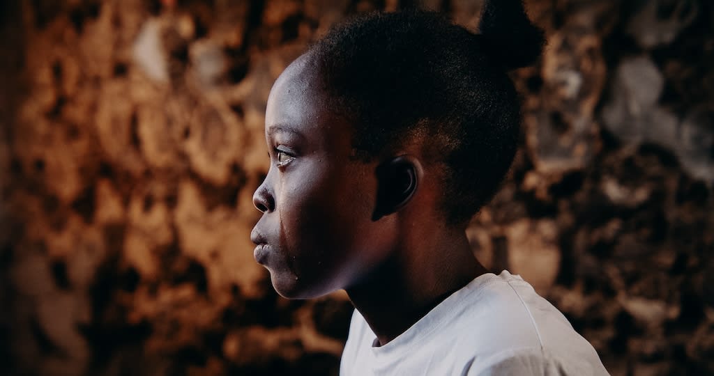 A young girl looks to the side with a tear running down her face. She is wearing a white shirt.