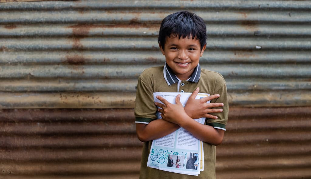 A boy in a green shirt is giving a hug to a letter that is clutched to his chest.