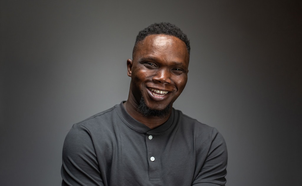 A man in a grey shirt smiles at the camera