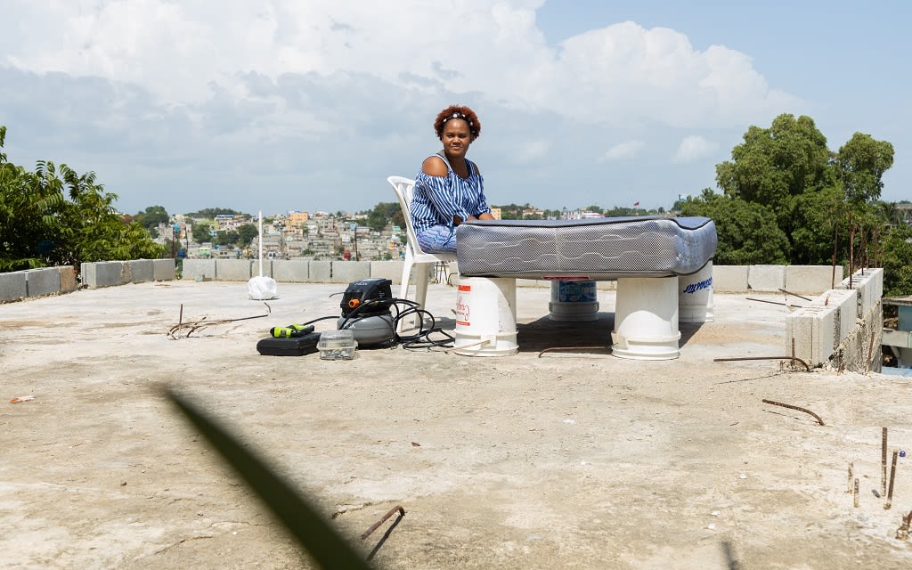 Yenny is sitting and working on a mattress-- a skill she learned through job skills training at her Compassion centre.