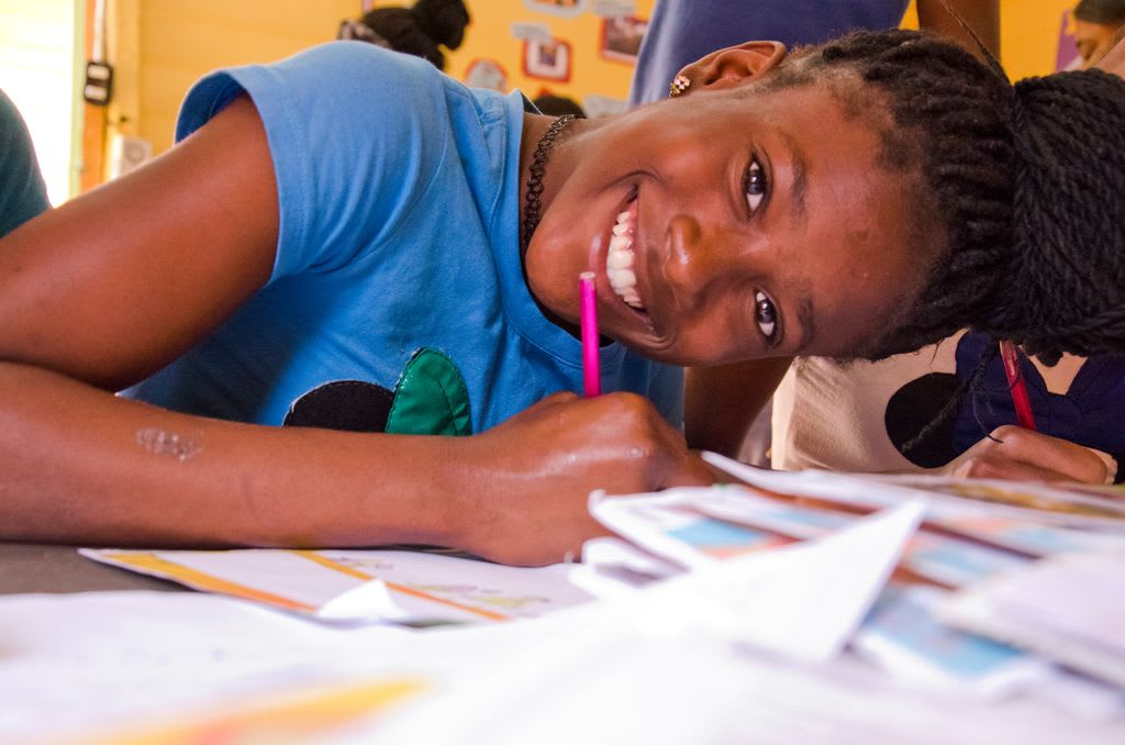 Arisleisy happily responds to a letter from her sponsor at her child development centre in the Dominican Republic. She is smiling big and wearing a blue shirt.
