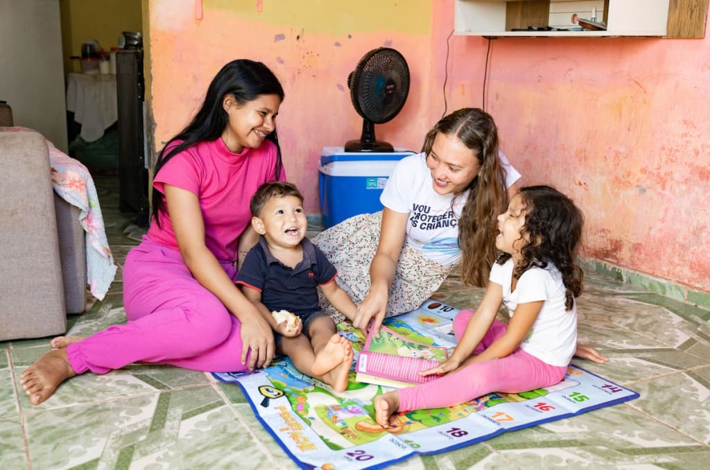 Gabrilla is sitting on the floor at home with her children and a visitor from the Compassion centre.