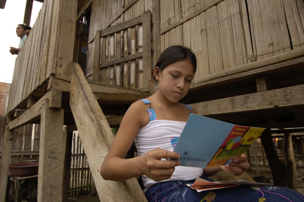 Little girl sits on the steps outside her home and reads a birthday card from her sponsor.