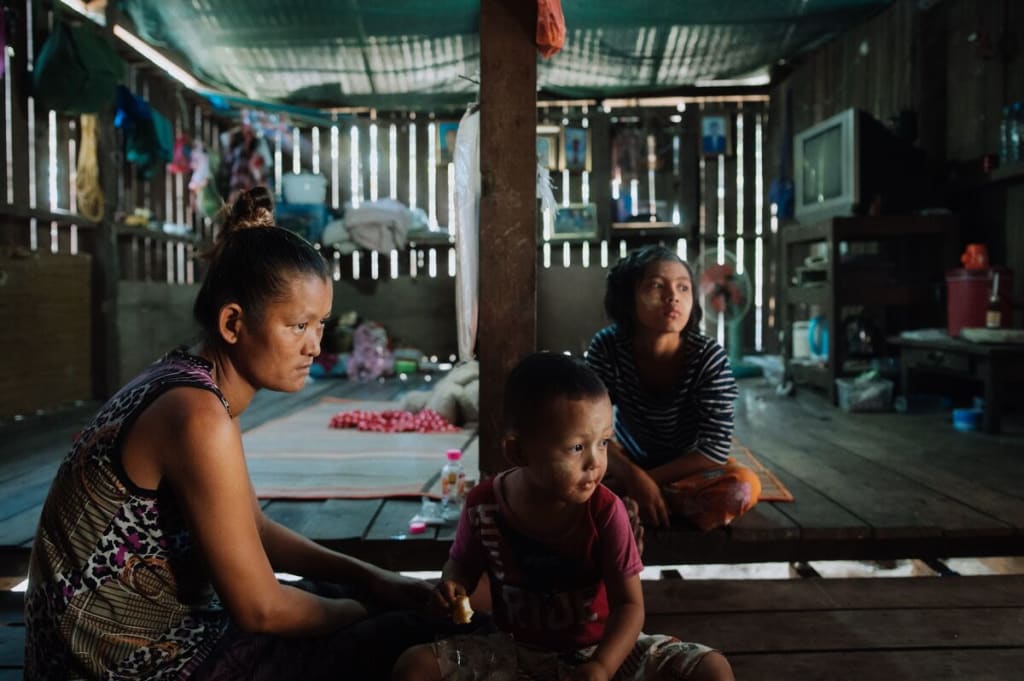 A family (mom, daughter and baby son) sit on the floor of their home.