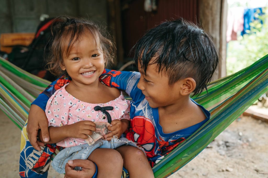 A brother lies in a hammock, holding his younger sister in his lap.