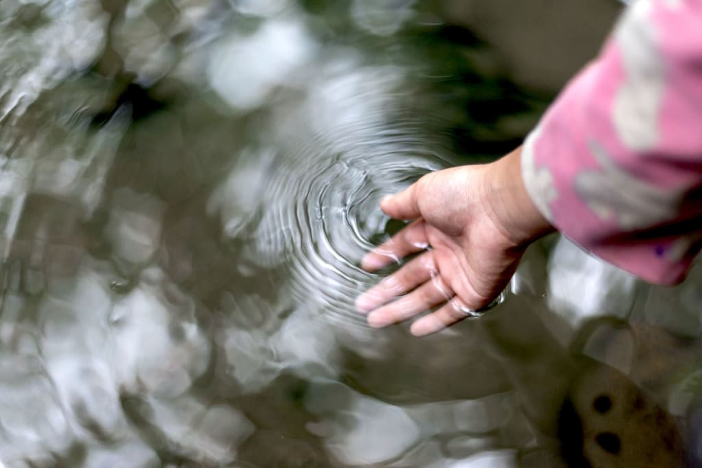 A woman dips her hand into a still body of water.