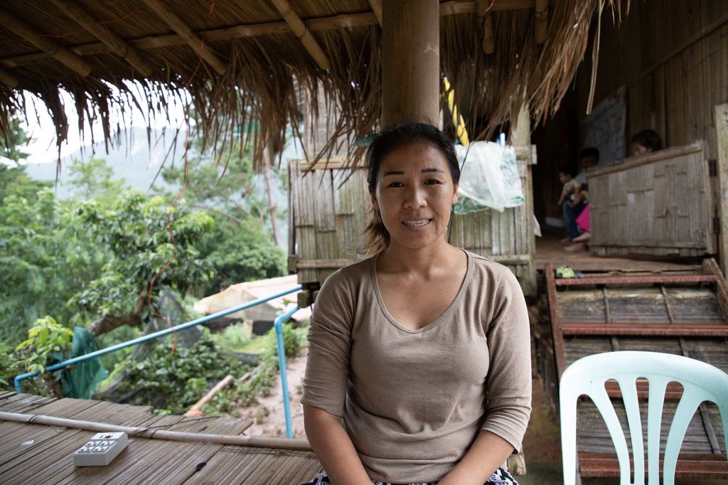 A woman in a tan shirt sits on the floor of a bamboo open-air room.