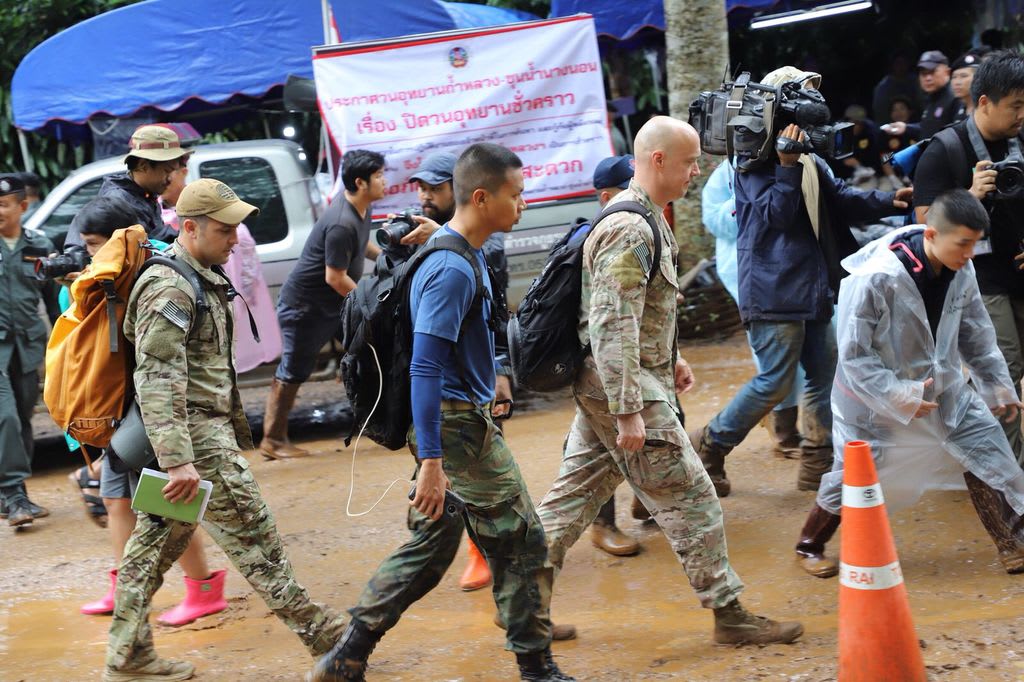 Three men walk down a road wearing camouflaged uniforms.