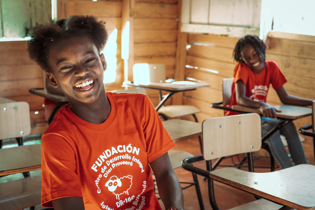 Lauri and her younger sister, Laurelis, are both sitting in desks at the Compassion centre. They are wearing orange shirts.