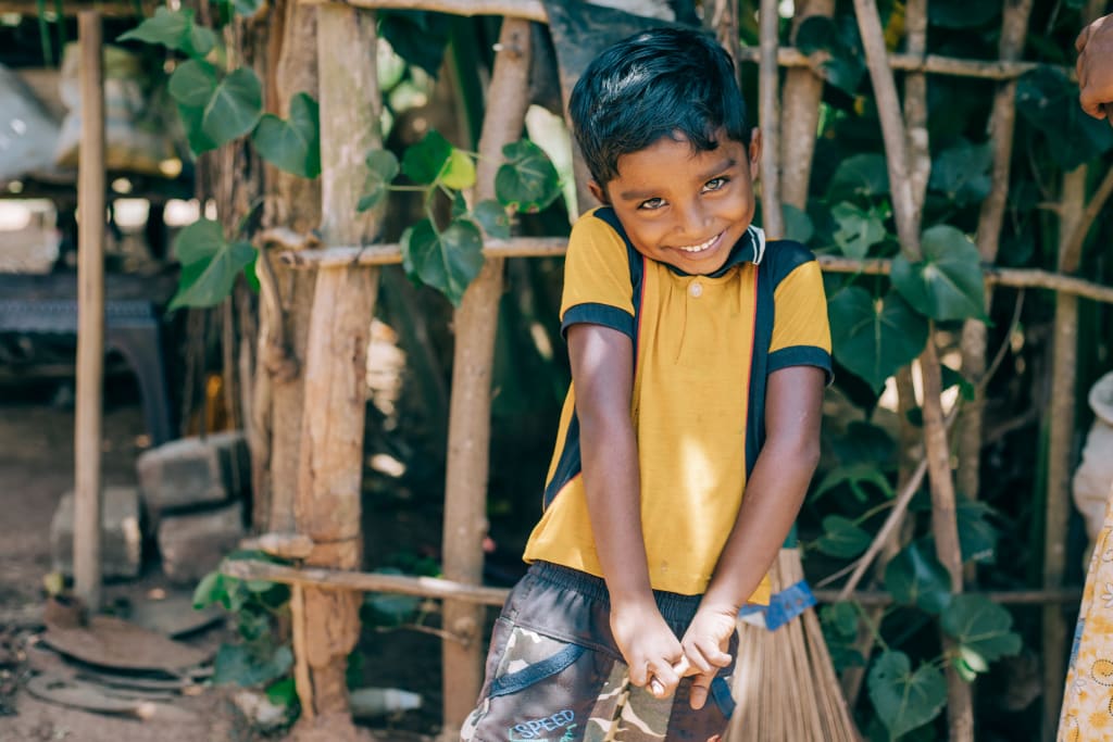 A little boy in a yellow shirt bashfully smiles.
