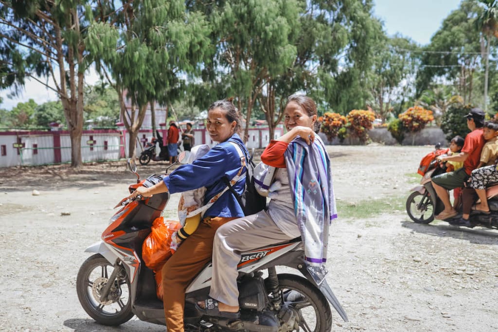 Serli is on her motorcycle carrying her baby, Nara. Jeni is riding on the back of the bike with her baby, Fhendy.
