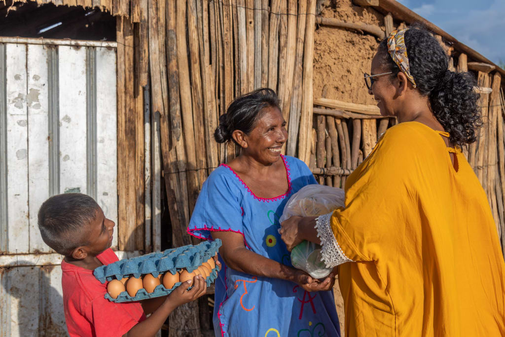 A woman and her son stand in front of their home made of sticks and corrugated metal They gratefully receive a gift of food - eggs, grain, oil and meat. They are one of many families experiencing the global food crisis.
