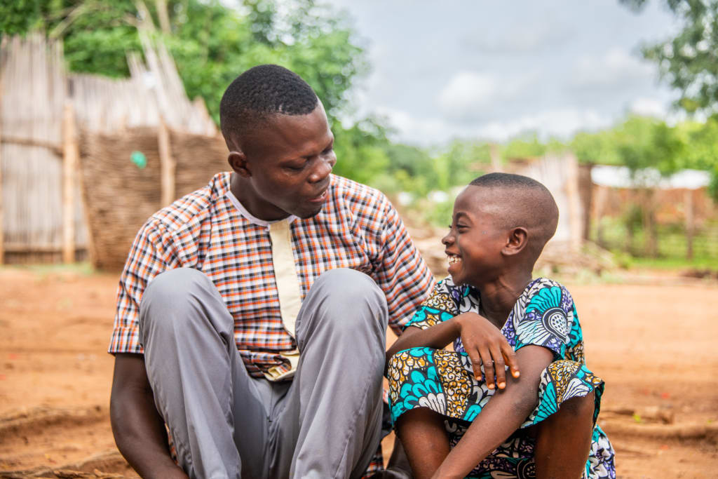 A man and a child sit together. The child is laughing while looking at the man.