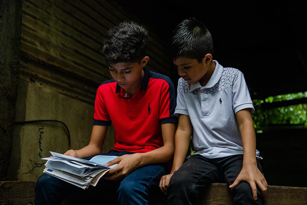 The boys read a letter together by their home.