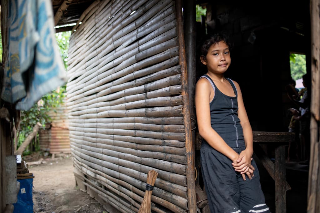 A girl in a black dress leans on the doorway of her home.