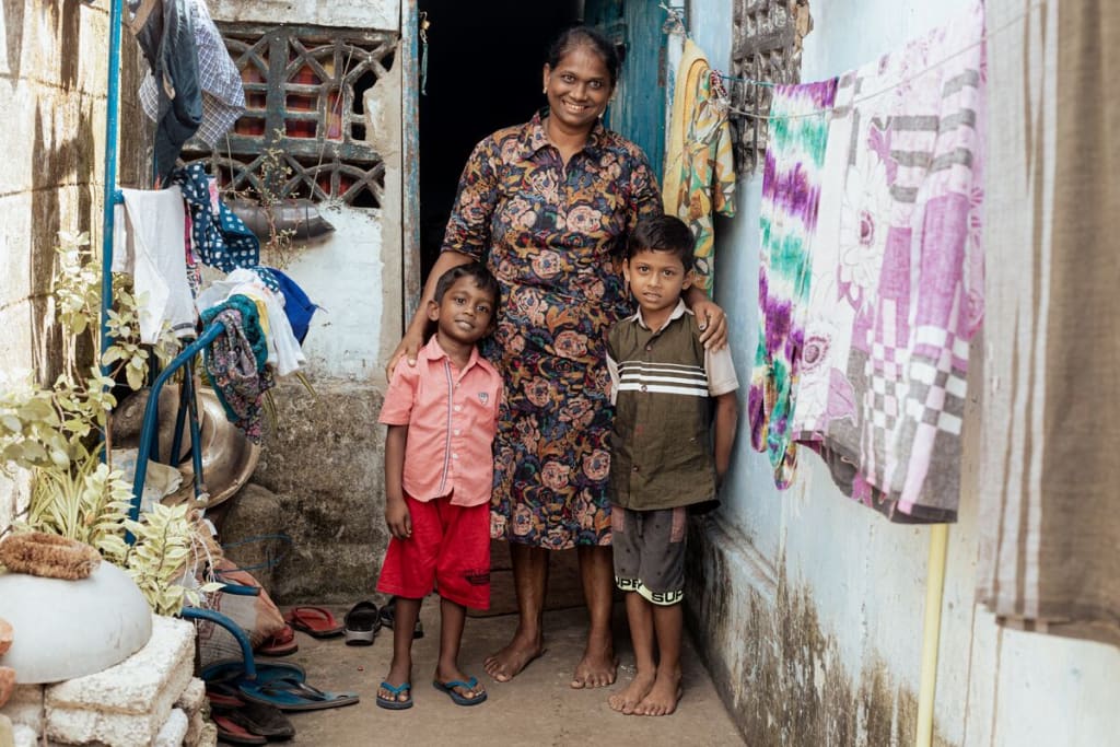 A woman in a patterned dress stands with her arms around two young boys.
