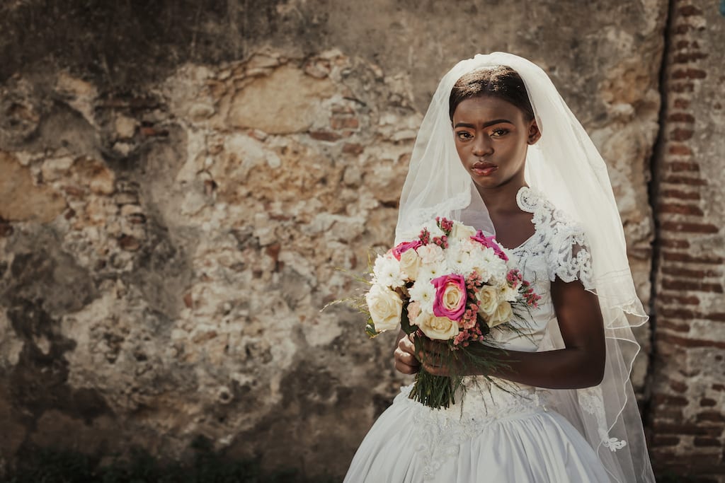 In a provocative protest against child marriage, Lauri is wearing a white wedding dress with a veil and she is holding a bouquet of flowers.