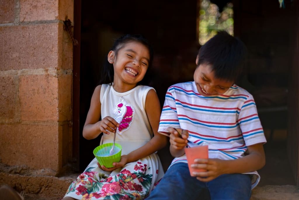 A little girl holding a bowl of ice cream sits with a boy holding a bowl of ice cream