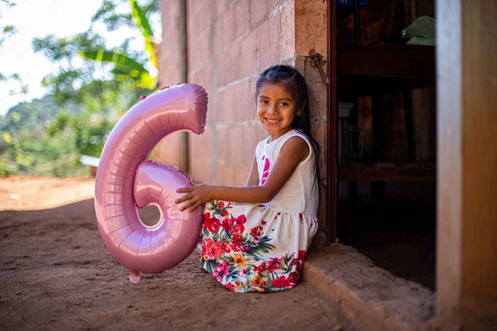 A girl in a colourful dress holds a balloon six