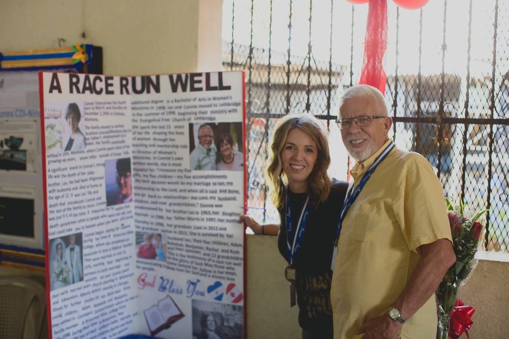 A man in a yellow shirt stands with a young woman in a black top beside a board that says "A race well run."
