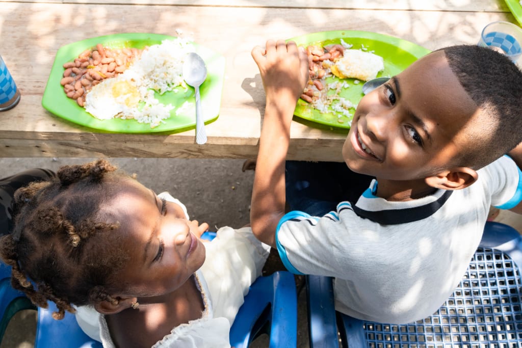 A girl and boy sit at a table with green plates of food in front of them and smile.