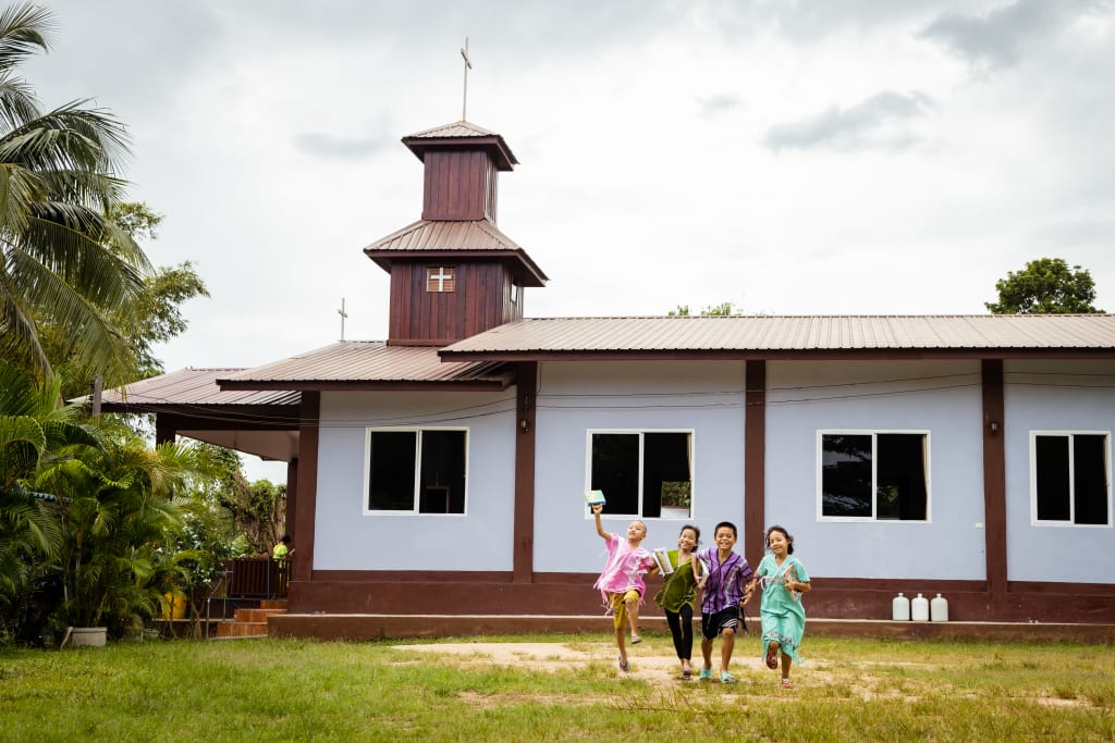 Four children run towards the camera with a church building in the background.