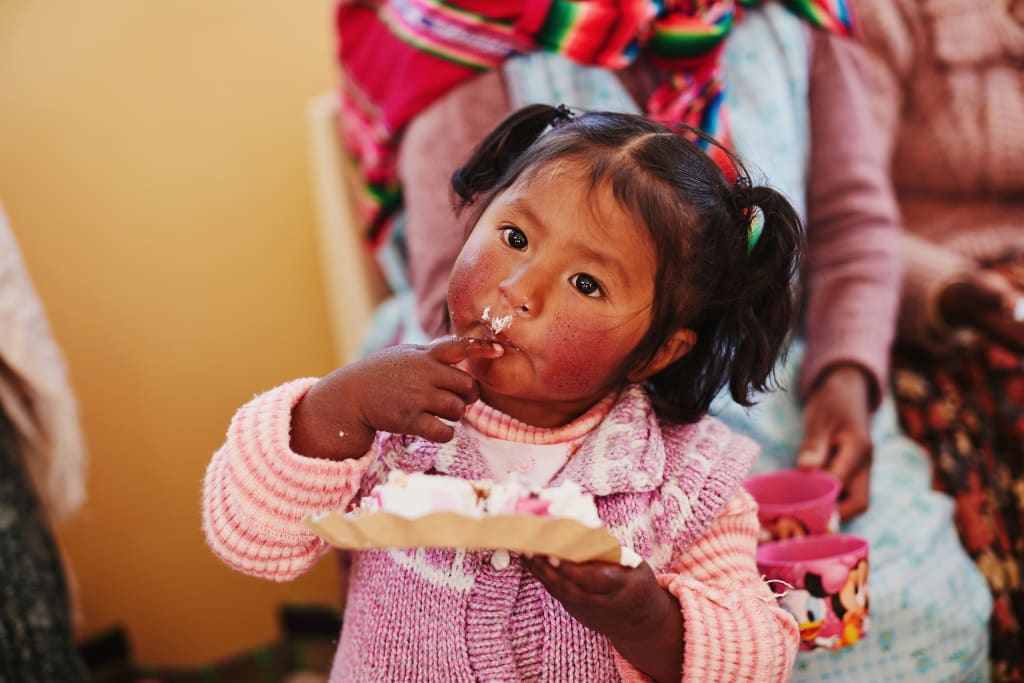 A girl wearing pink and purple licks icing off her fingers.
