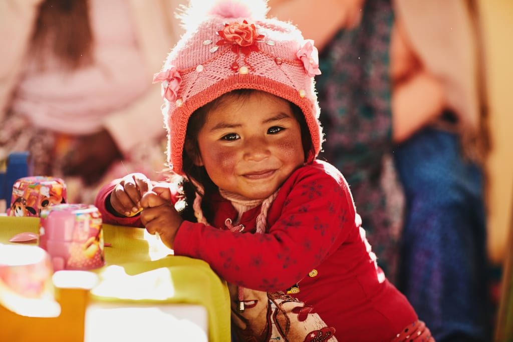 A girl wearing a pink hat and a red sweater smiles at the camera.