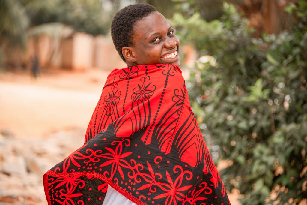 Adrienne is wearing a white skirt with a brown, red, and white shirt. She has a red and black cloth wrapped around her shoulders.