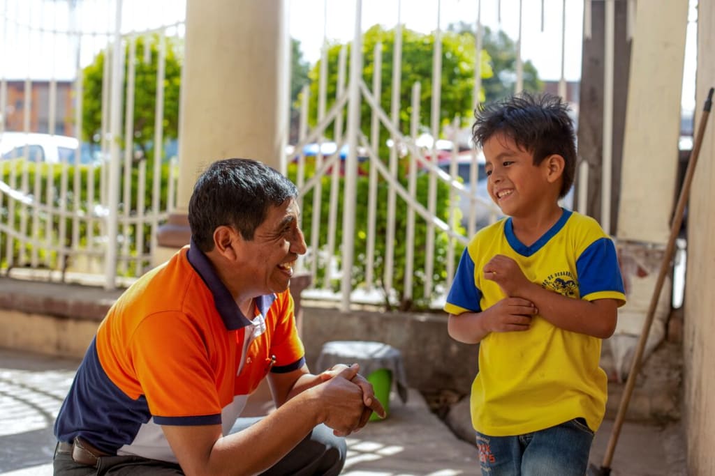 A man in an orange shirt smiles with a boy in a yellow shirt