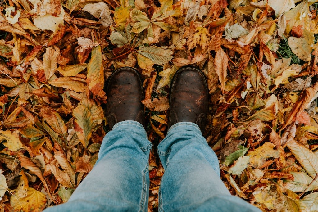 Photo by Hermes Rivera A man stands on red, orange and yellow leaves. He is wearing brown boots and blue jeans.