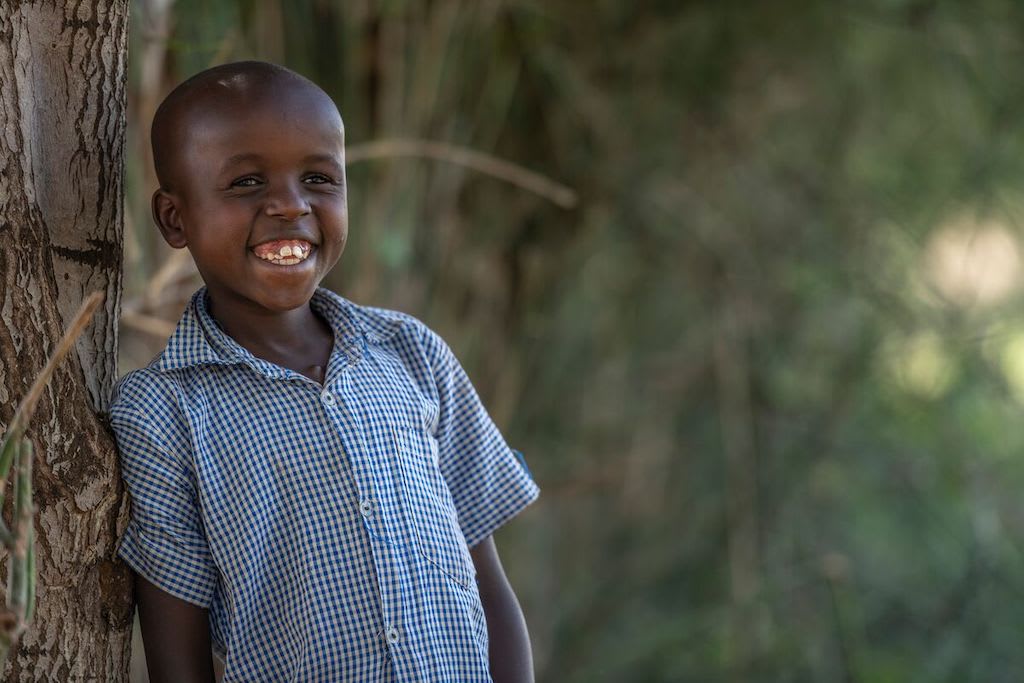 Brian leans against a tree, smiling and wearing a blue shirt.