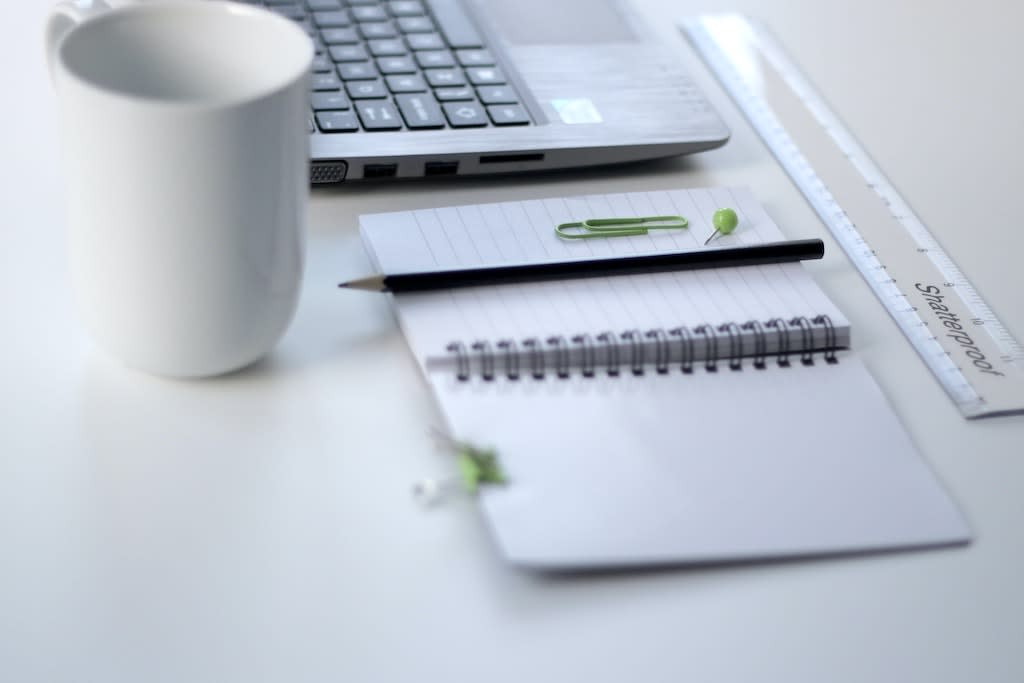 A desk with a laptop, notebook and mug on it.