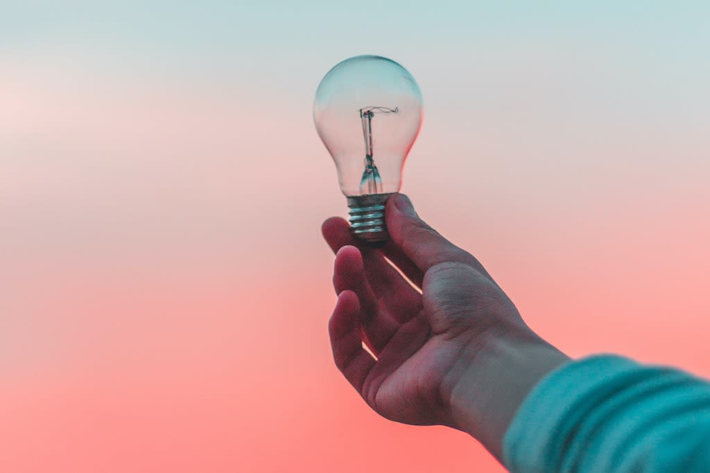 A hand holding a lightbulb to the sky.