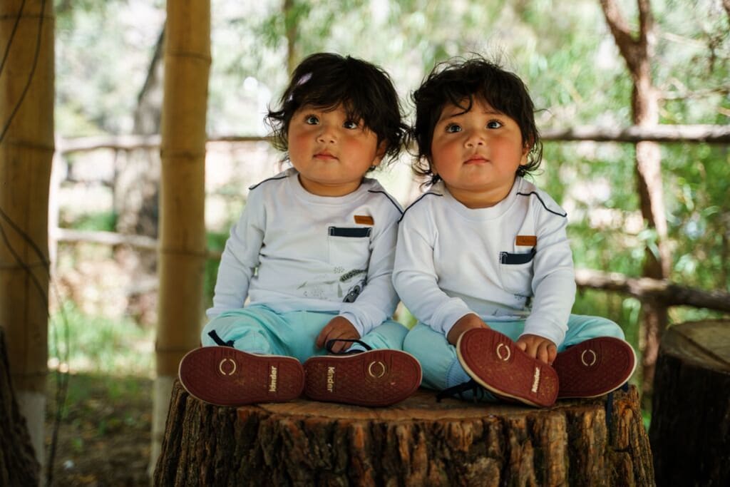 A pair of twins wearing the same outfits both look at the camera