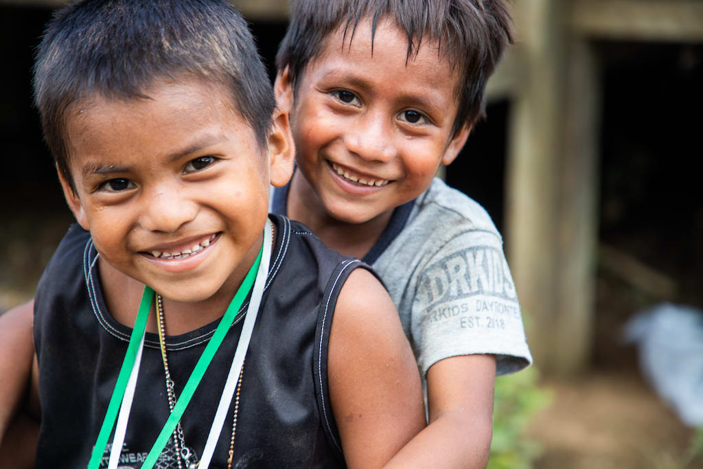 Two boys, one in a black tank top and one in a grey t-shirt, smile at the camera.