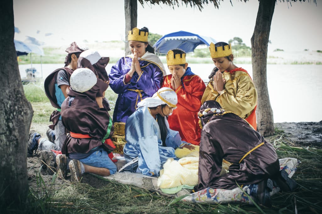 Children dressed in costume reenact the manger scene outside below palm trees