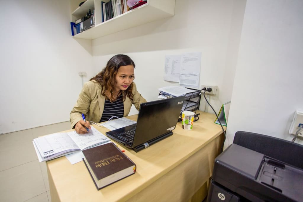 A woman is at a desk working on her laptop. The room is white.