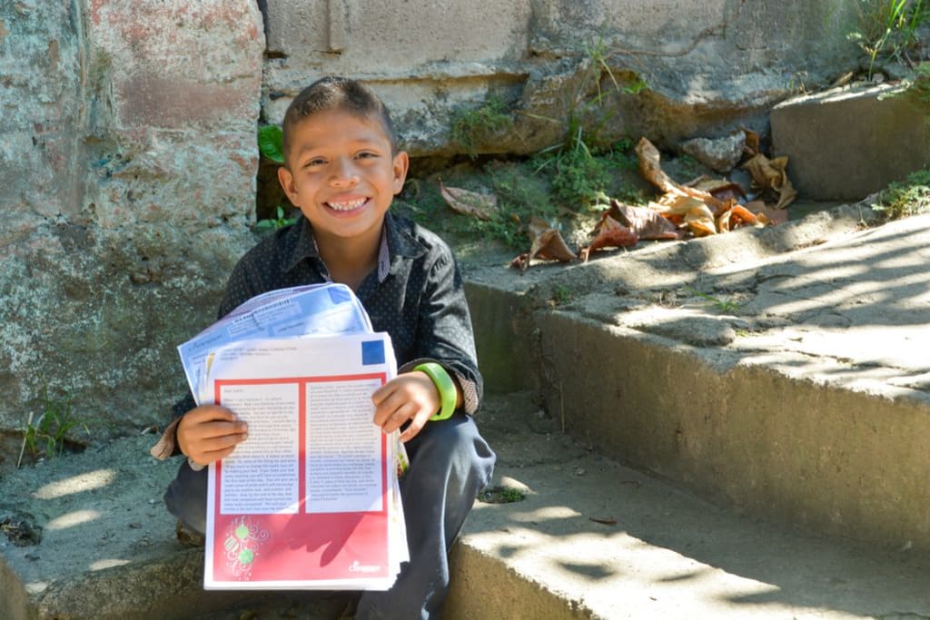 Justin, in El Salvador, proudly shows off a stack of letters from his sponsor. He has a big smile.